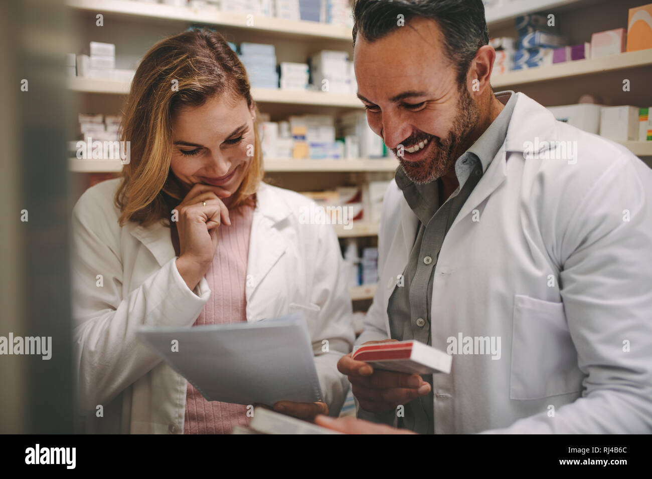 Two dedicated male and female pharmacists looking for the best medicine in the stock while working together in a pharmacy. Pharmacists holding prescri Stock Photo
