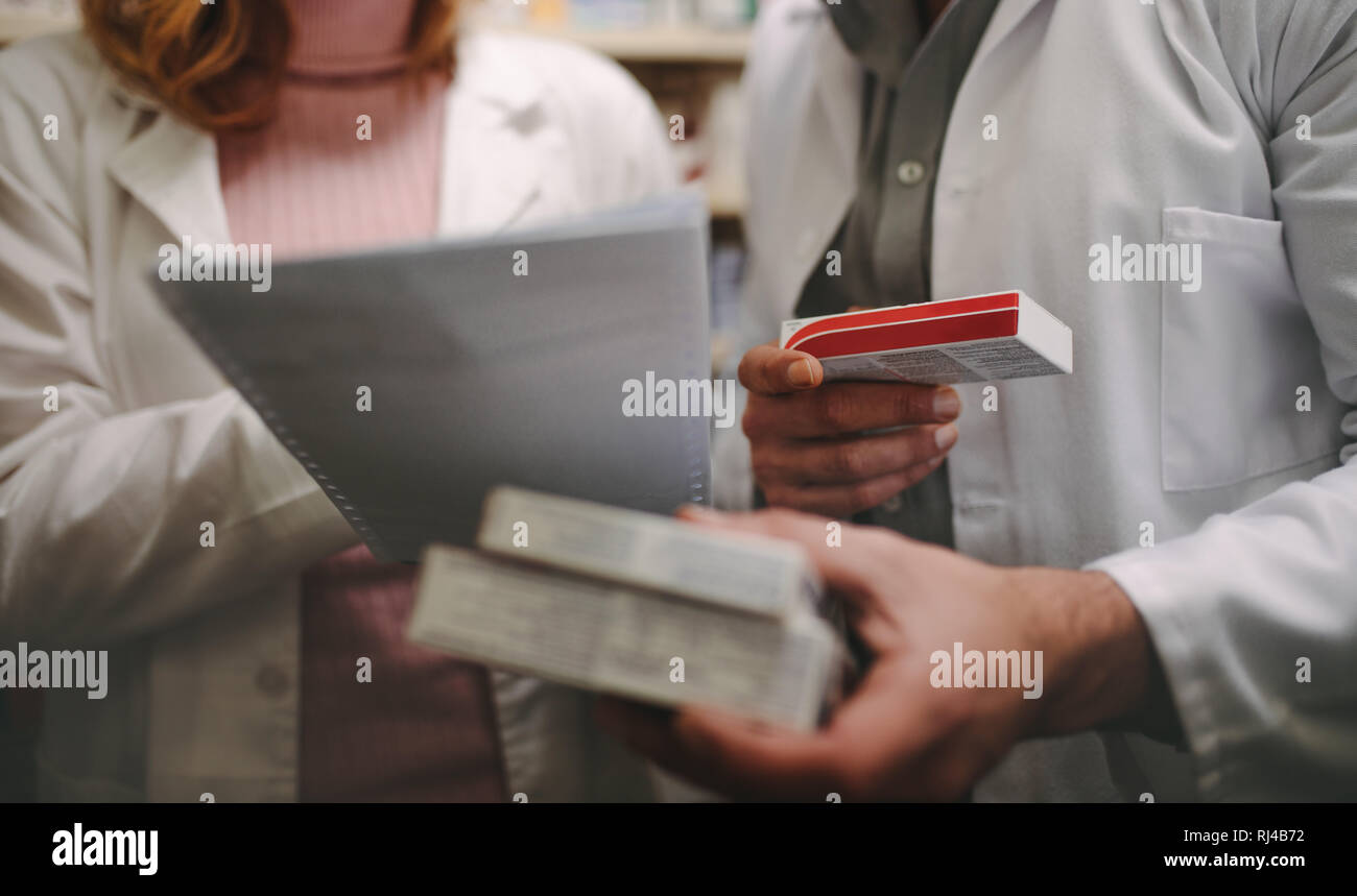 Two chemist with a prescription searching right medicine in pharmacy store. Female pharmacist holding prescription  with male checking medicine in pha Stock Photo