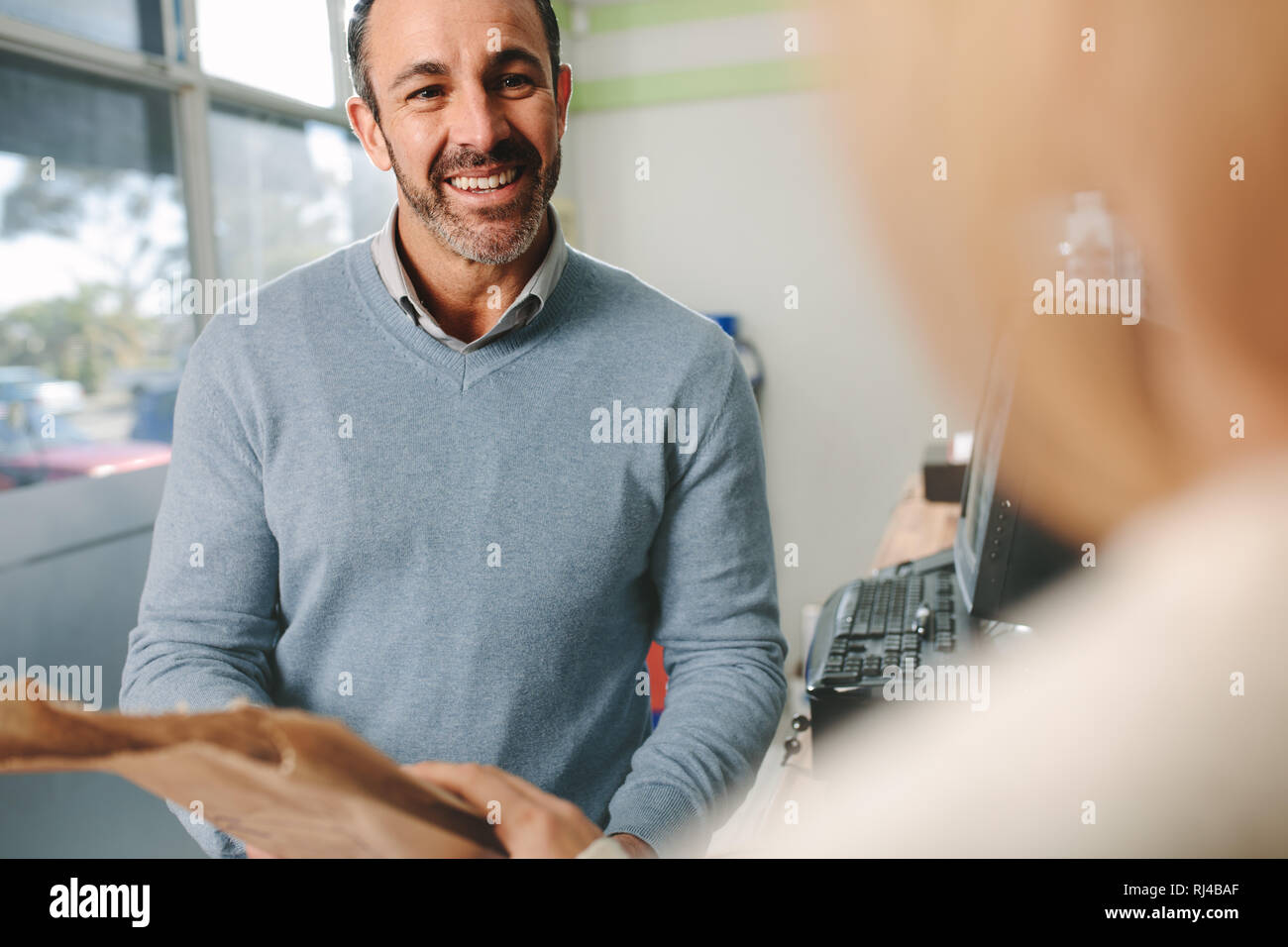 Male drug store employee giving medicine to customer at checkout counter. Pharmacist dealing with customer at pharmacy. Stock Photo