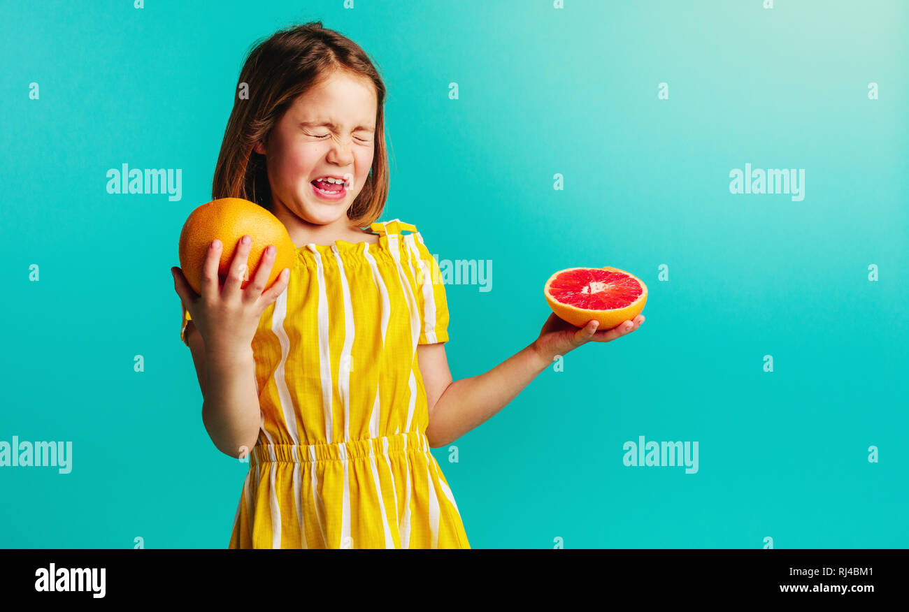 Caucasian girl child with grapefruit on a blue background. Girl does not like the taste of grapefruit. Stock Photo