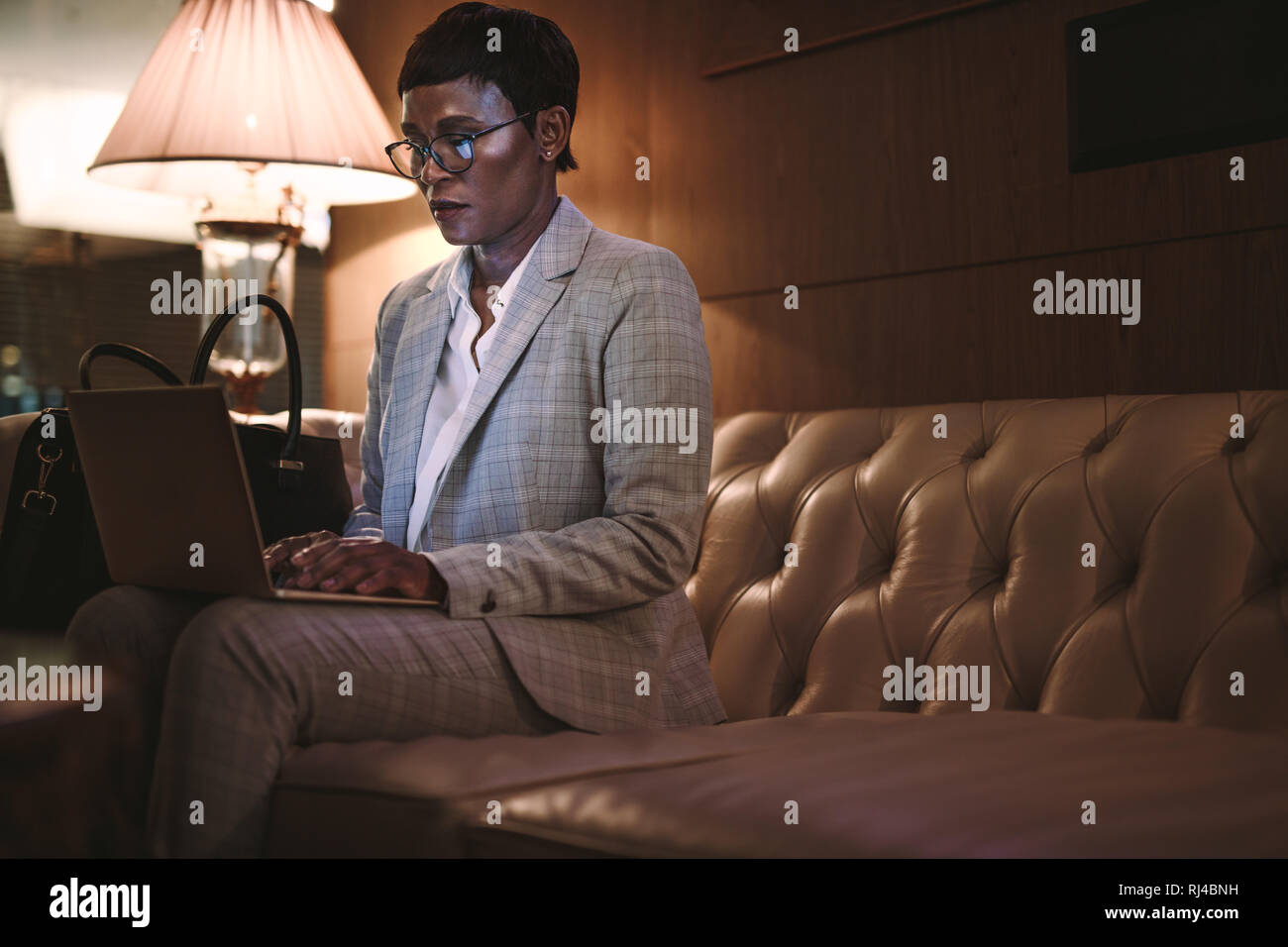 Businesswoman sitting at hotel lobby and working on laptop. African female CEO on business tour using laptop in hotel lobby. Stock Photo