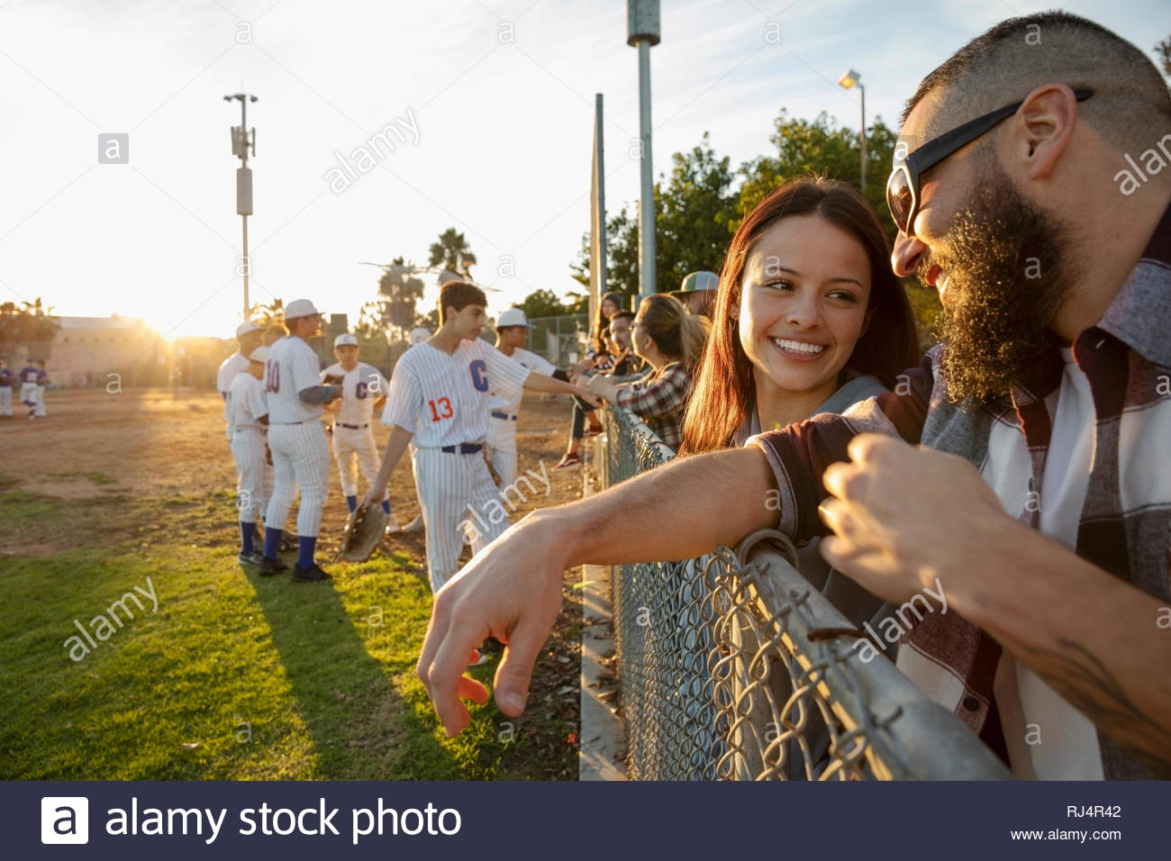 Father and daughter talking, watching baseball game at fence Stock
