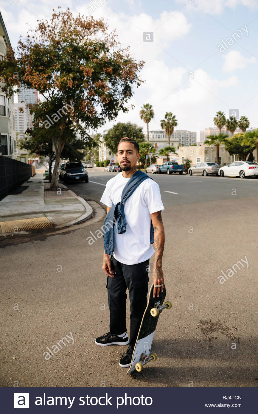 Portrait confident, cool Latinx young man with skateboard on urban ...