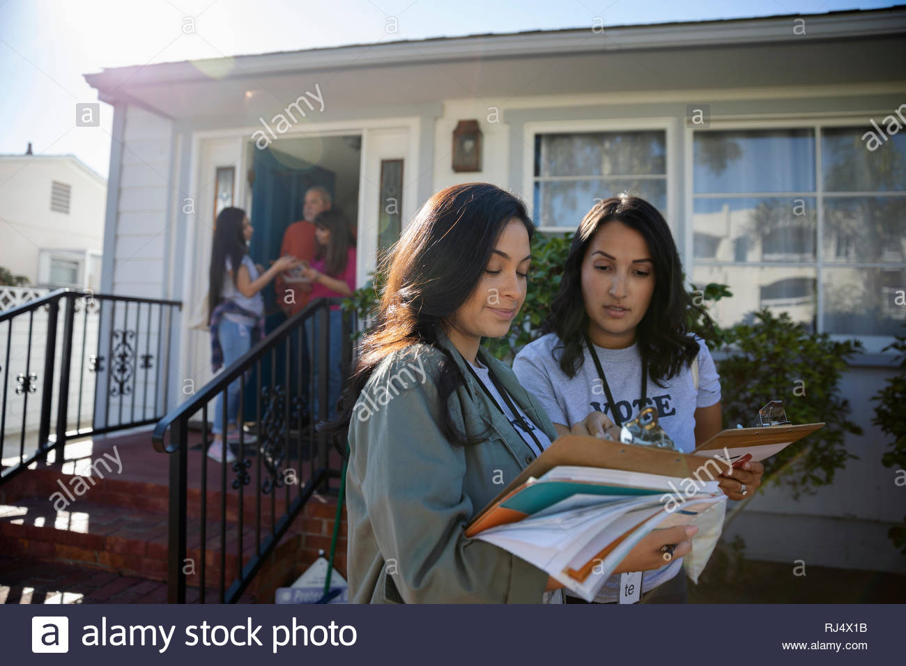 Latinx Female Volunteers With Clipboards Canvassing Door To