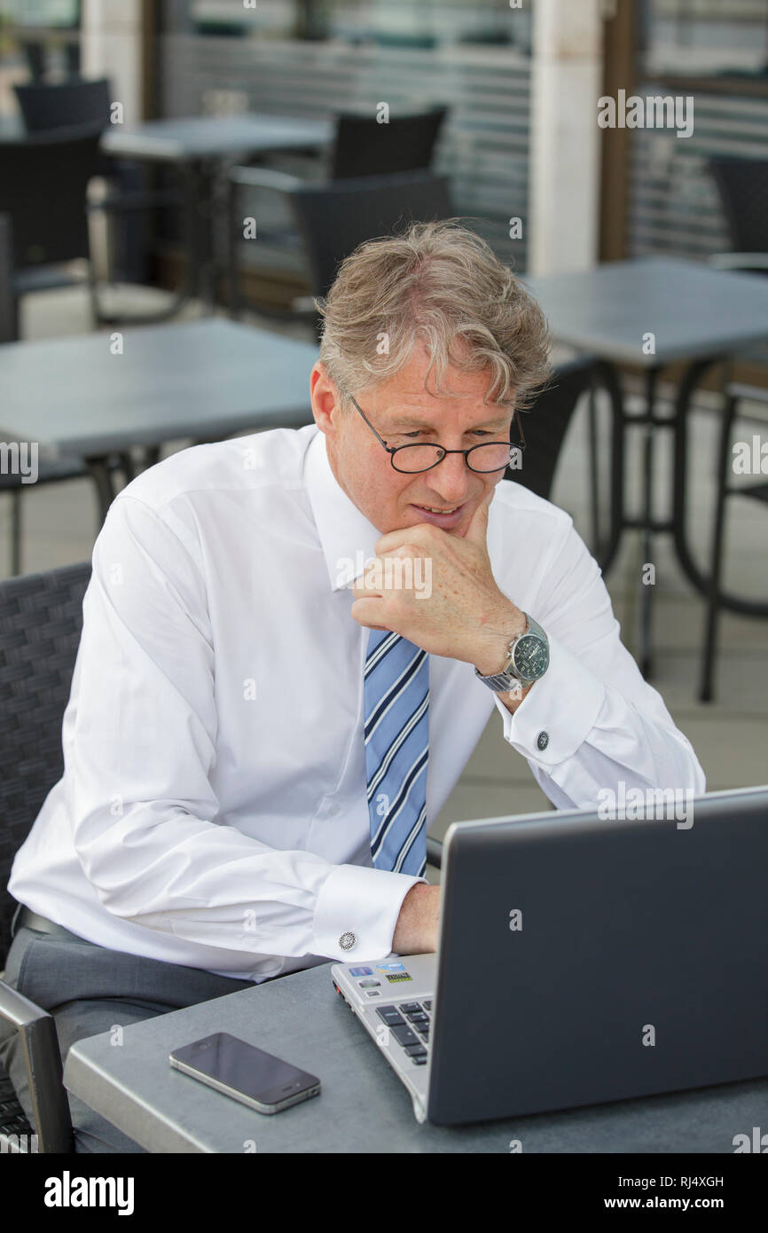 Geschäftsmann mit Laptop und Telefon am Tisch in Straßenrestaurant Stock Photo