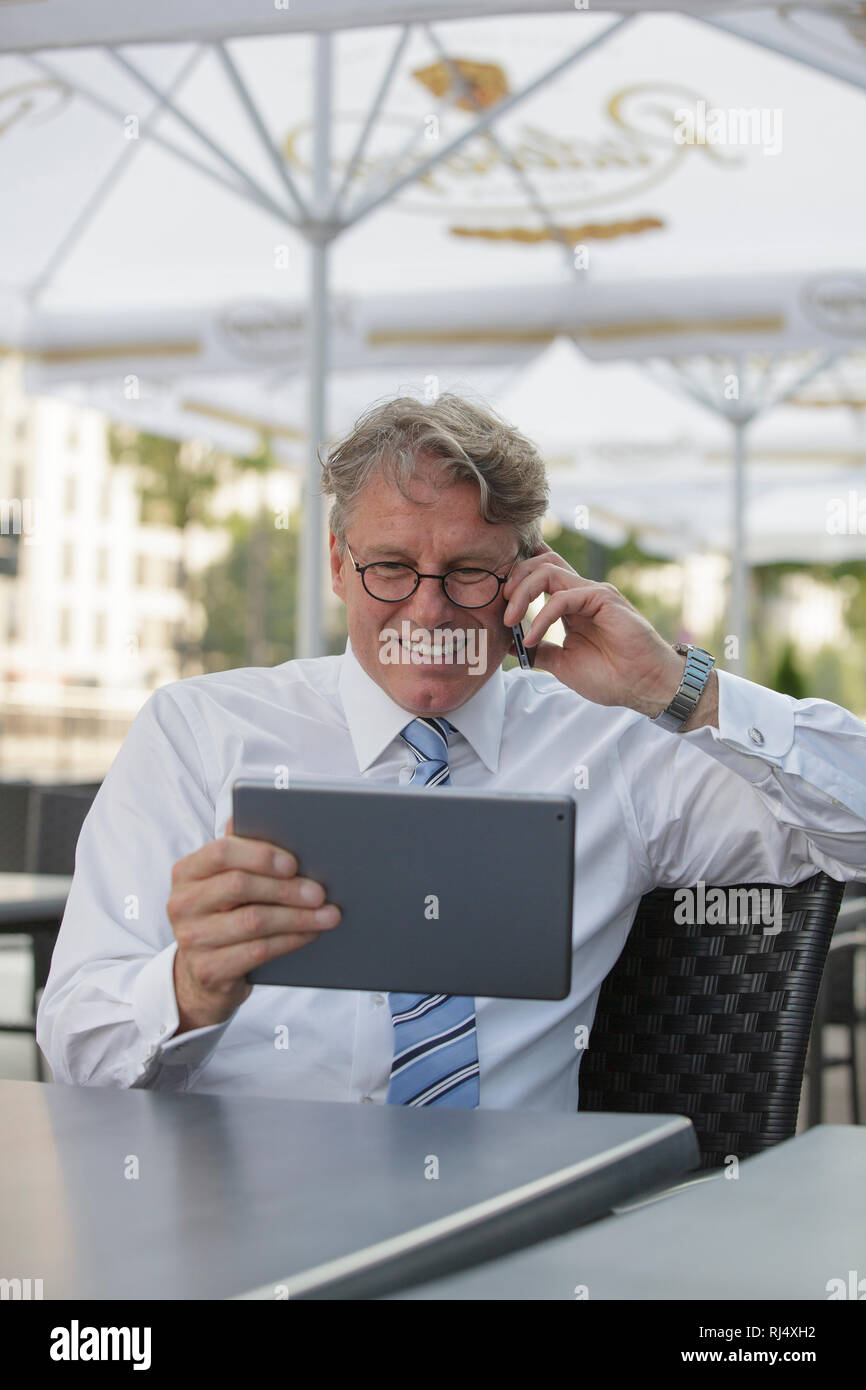 Geschäftsmann mit iPad sitzt am Tisch in Straßenrestaurant Stock Photo