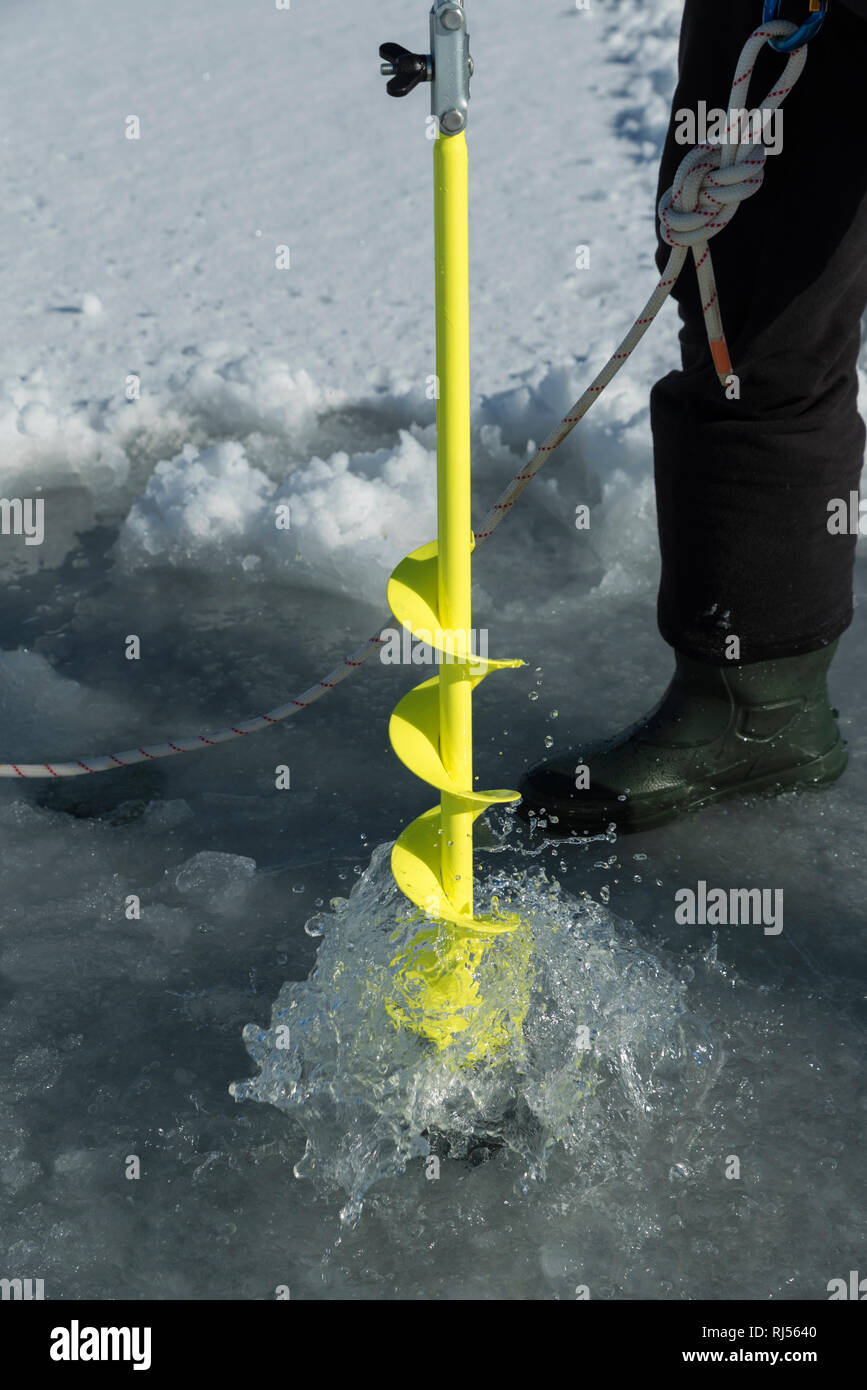 Detailed vertical image of ice auger drill drilling a hole in a frozen