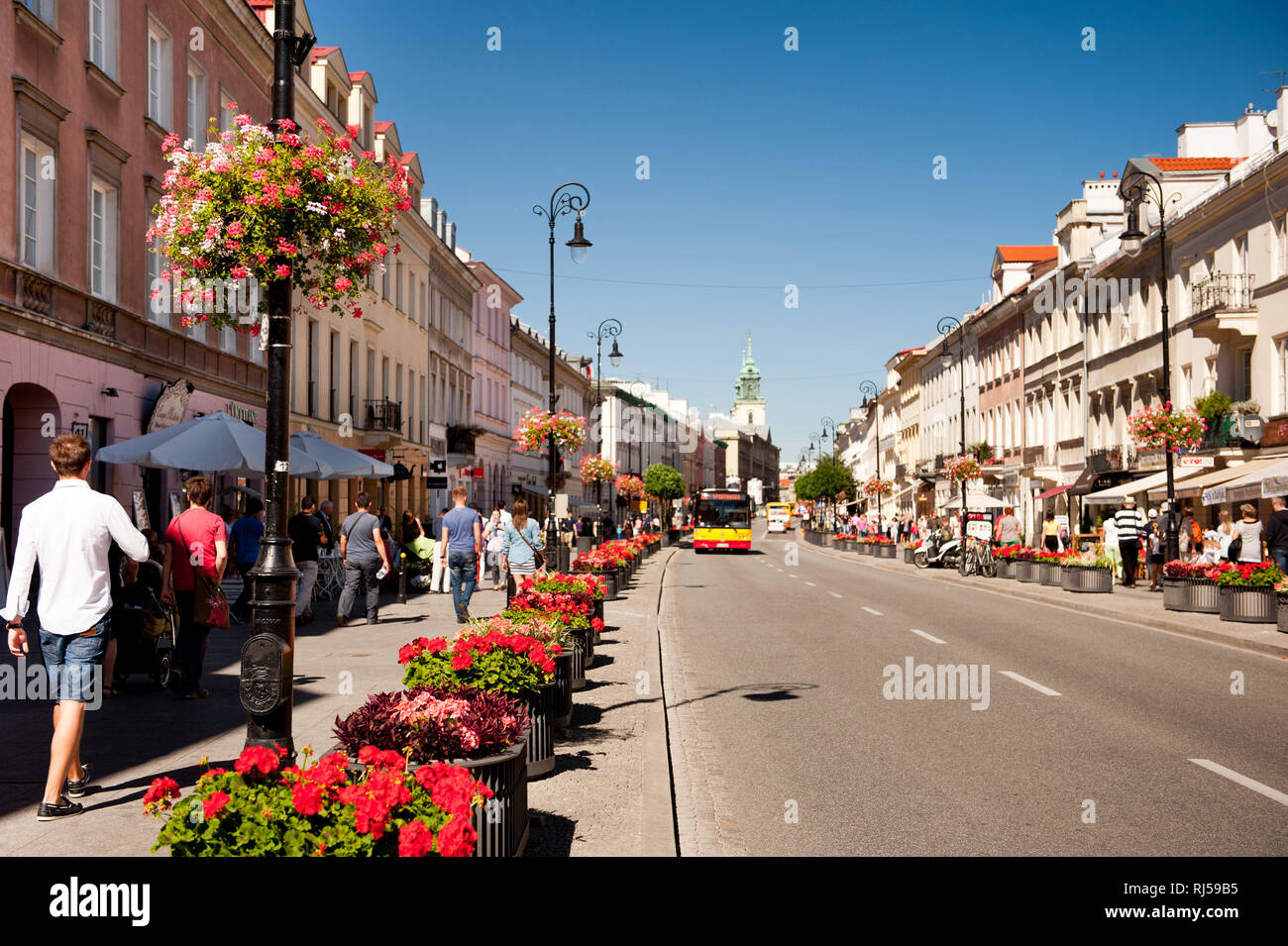 Red geranium flowers planted along street, people walking on sidewalk at Nowy Swiat in Warsaw, Poland, summertime, Stock Photo