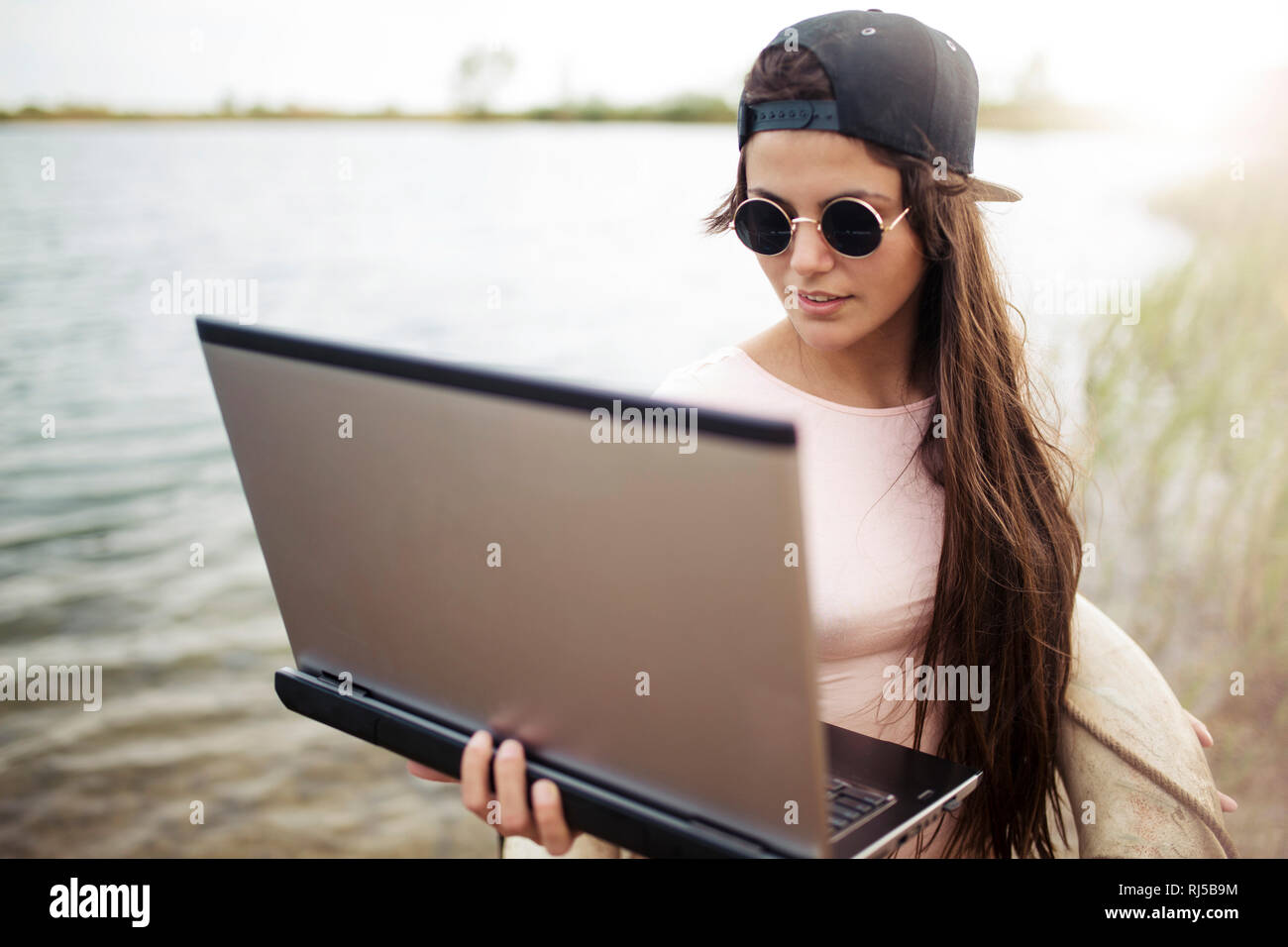 junge Frau steht mit Laptop am Strand Stock Photo
