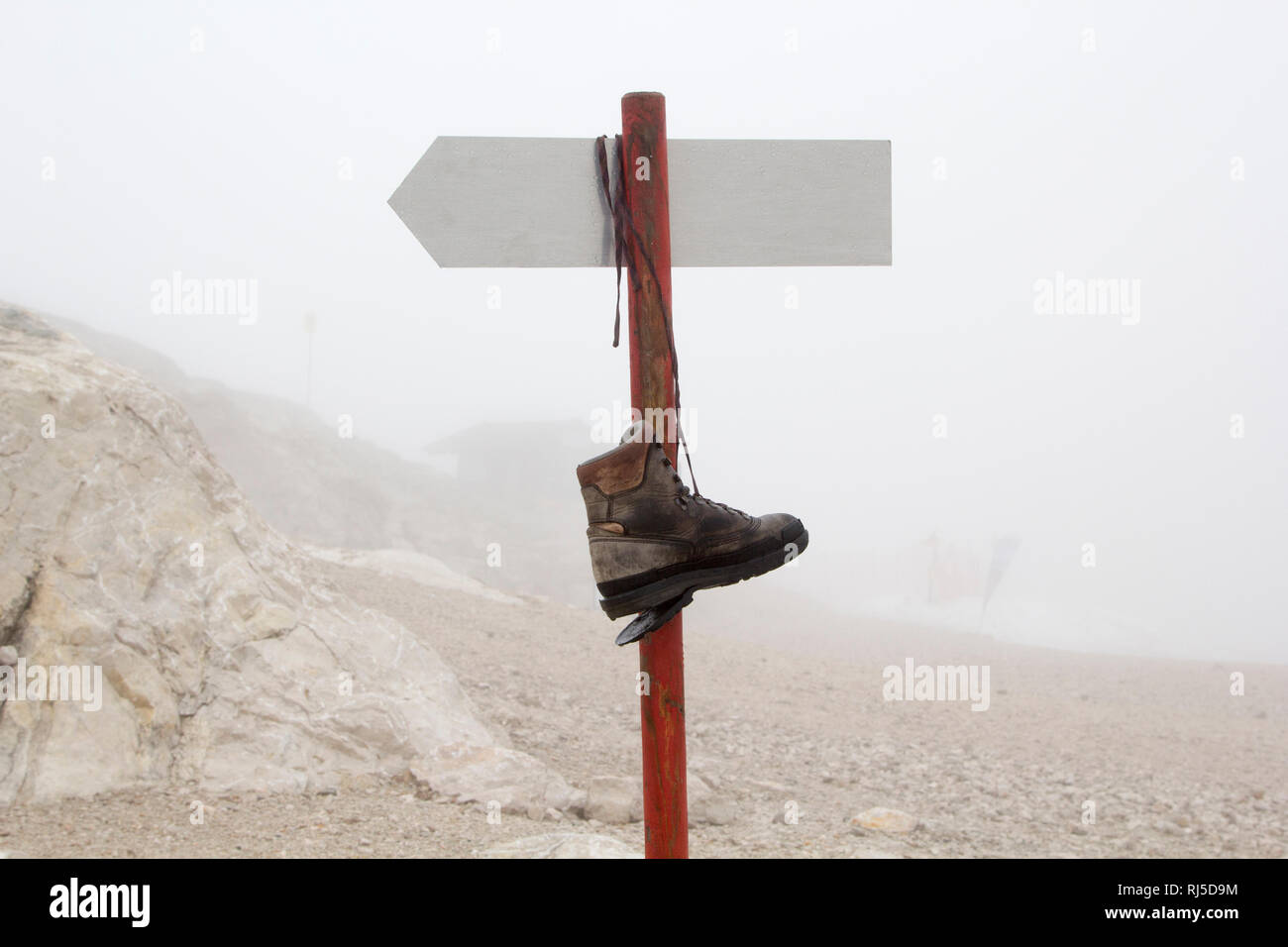 Ein kaputter Bergschuh hängt auf einem Berg an einem Wegweiser im Nebel Stock Photo