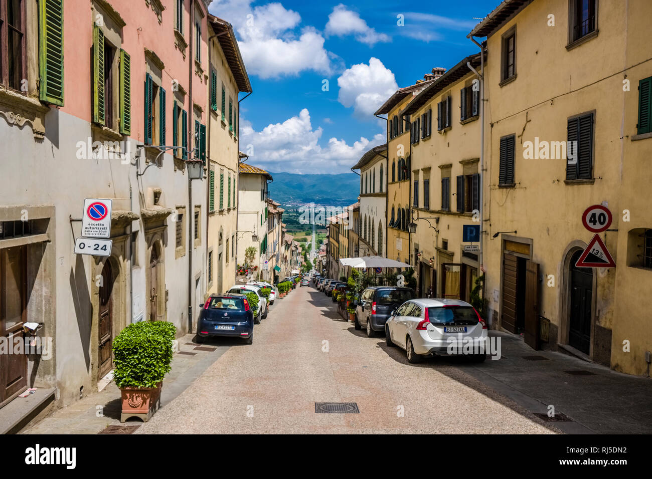 Straight road leading down from medieval town to typical hilly Tuscan countryside with fields and trees Stock Photo
