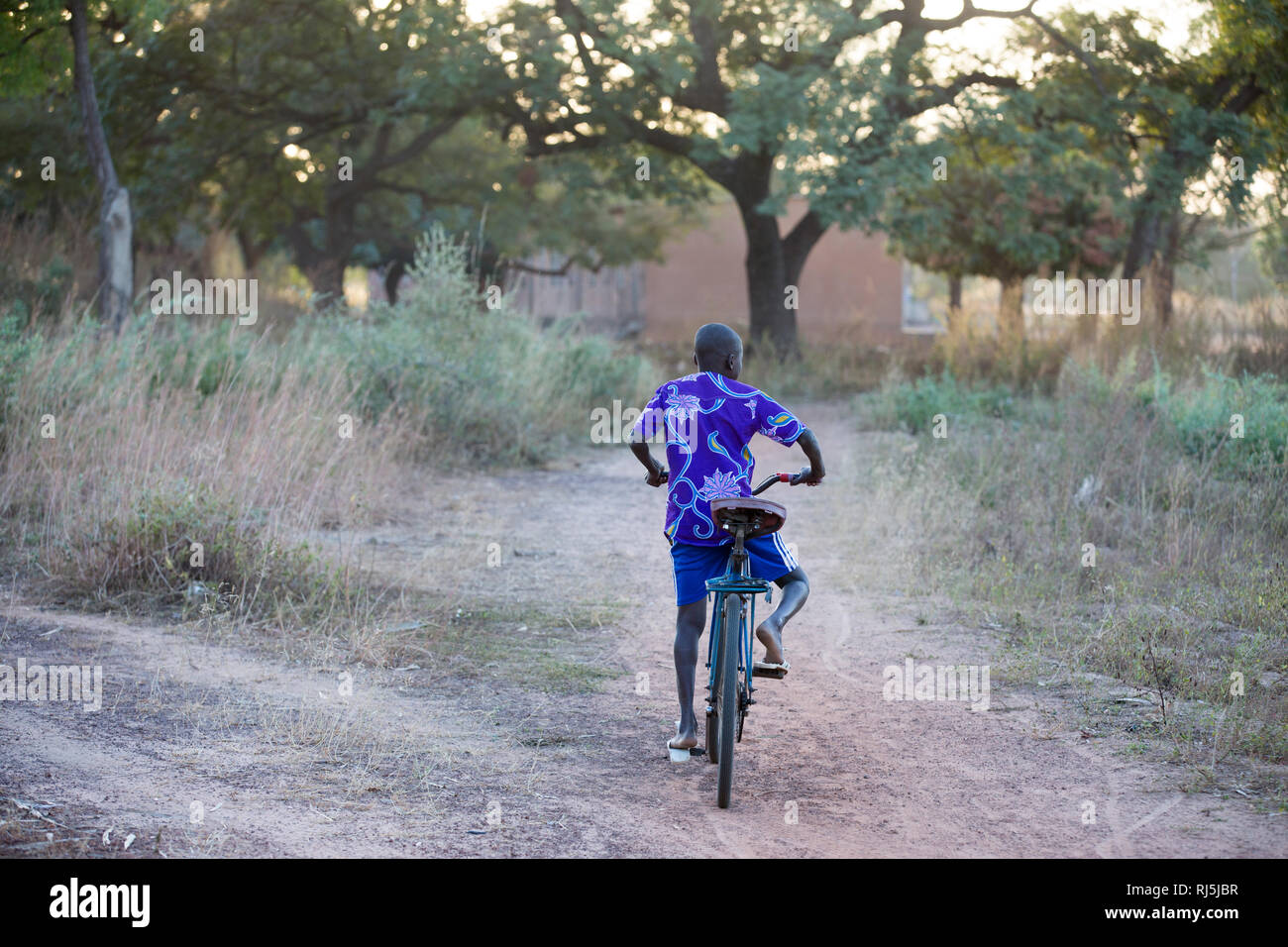 Bodadiougou village, Banfora, Cascades Region, Burkina Faso, 4th December 2016; A boy on his bike cycling through the village. Stock Photo