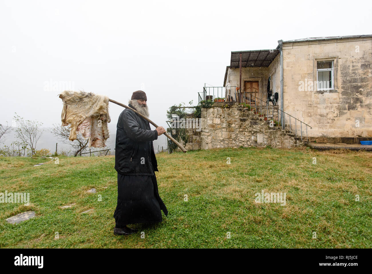 Dieser Priester hat gerade ein Schaf geschlachtet und bringt das Fell jetzt ins Haus um es zu trocknen. Roadtrip durch Georgien im Oktober 2016. Stock Photo