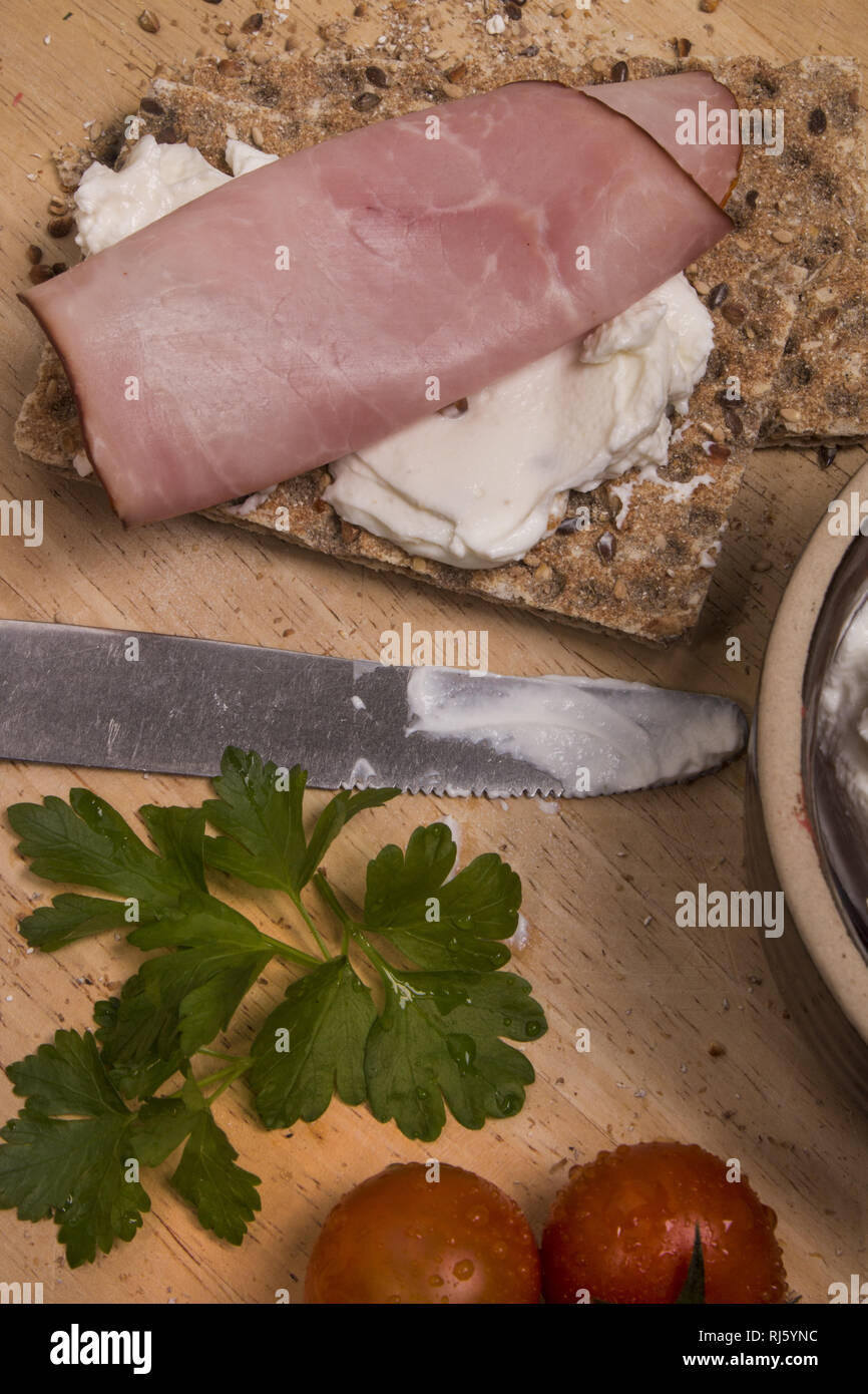 healthy breakfast with crispbread, quark, parsley and smoked ham on a wooden board Stock Photo