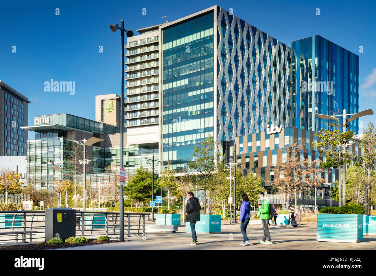2 November 2018: Salford Quays, Manchester, UK - ITV and BBC buildings on a sunny autumn day, clear blue sky, colourfully dressed young people in... Stock Photo