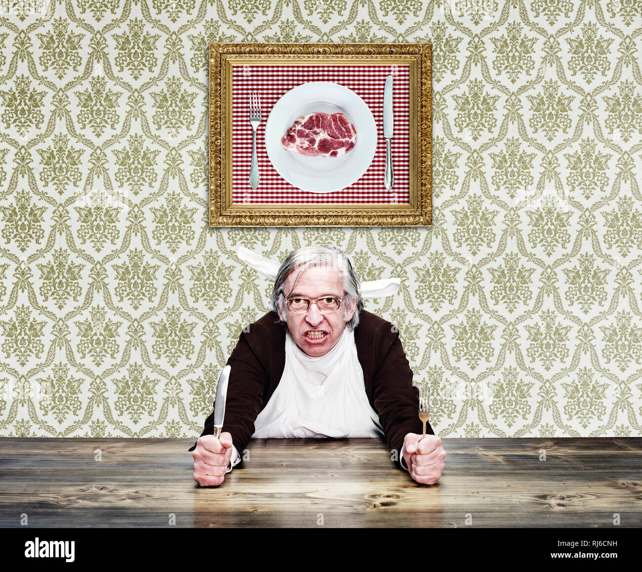 Mann mit grauem Haar und Brille am Tisch, hält Messer und Gabel in den Händen, Foto mit Fleisch an der Wand Stock Photo