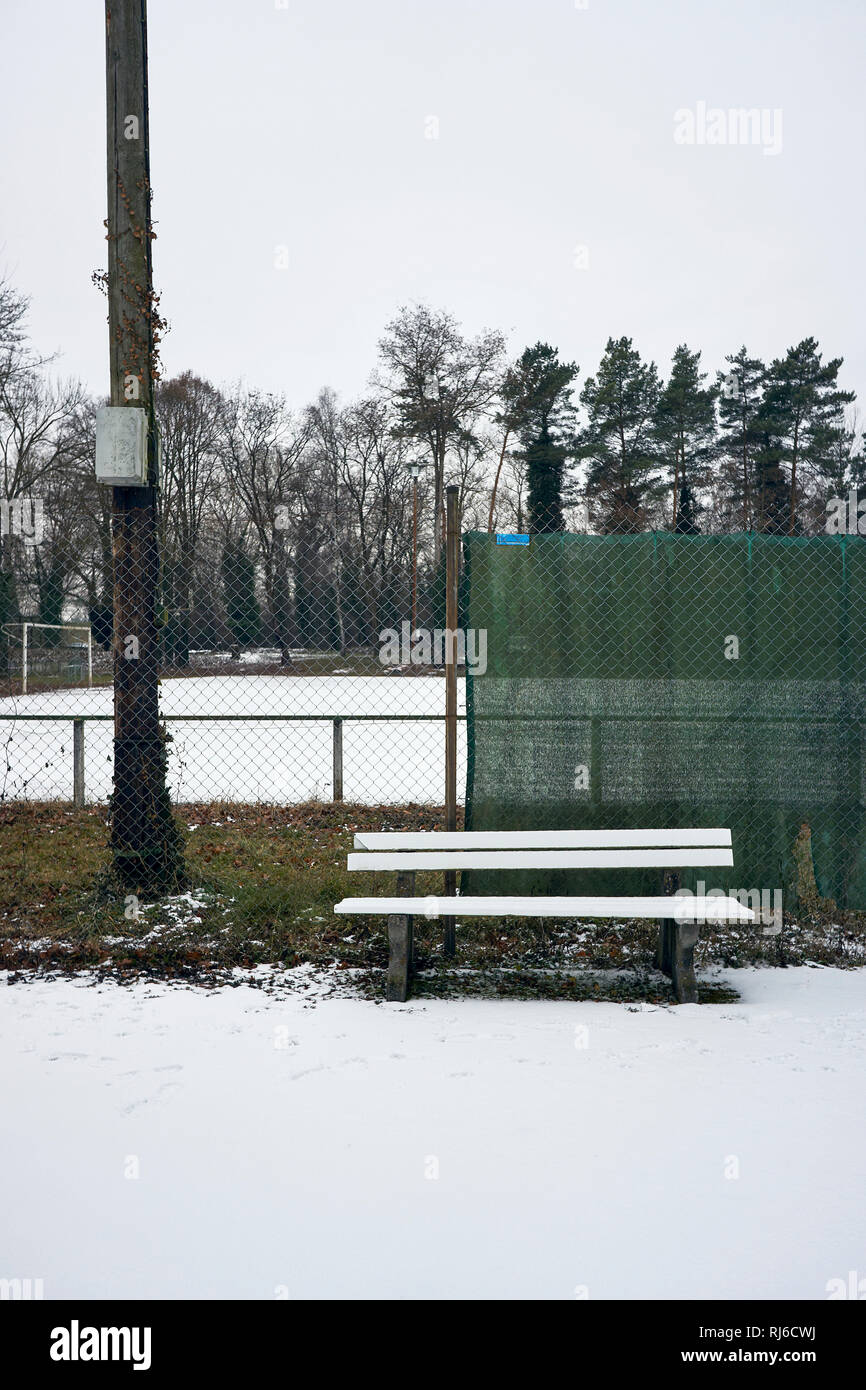 verschneite Bank an Zaun vor einem Fußballplatz im Winter, Stock Photo
