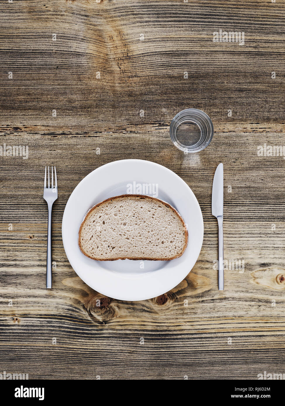 eine Seine Brot auf Teller, Besteck und Glas auf altem Holztisch, von oben Stock Photo