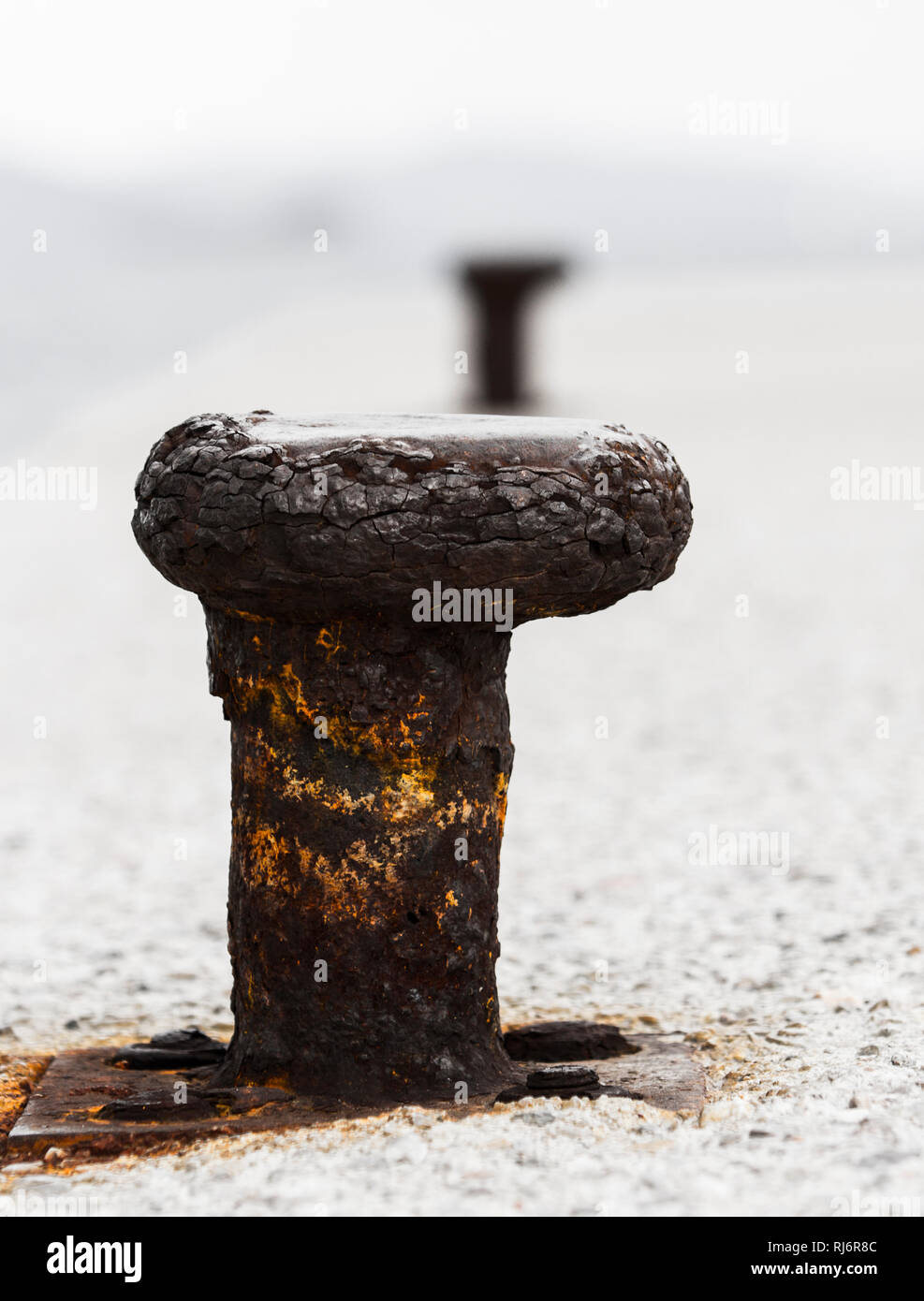Close-up profile of worn-out rusted bollard in perspective with another one. Erosion of trust concept with copy space. Stock Photo
