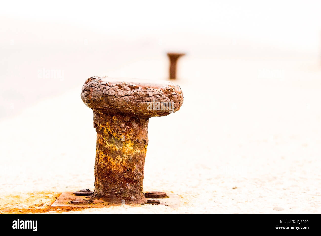 High-key image of worn-out rusted bollard in perspective with another one. Erosion of trust concept with copy space. Stock Photo