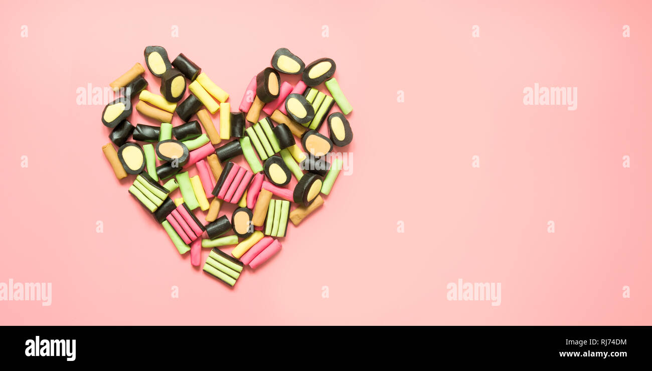 Shape of heart. Colorful lollipop and licorice candy on pink. View from