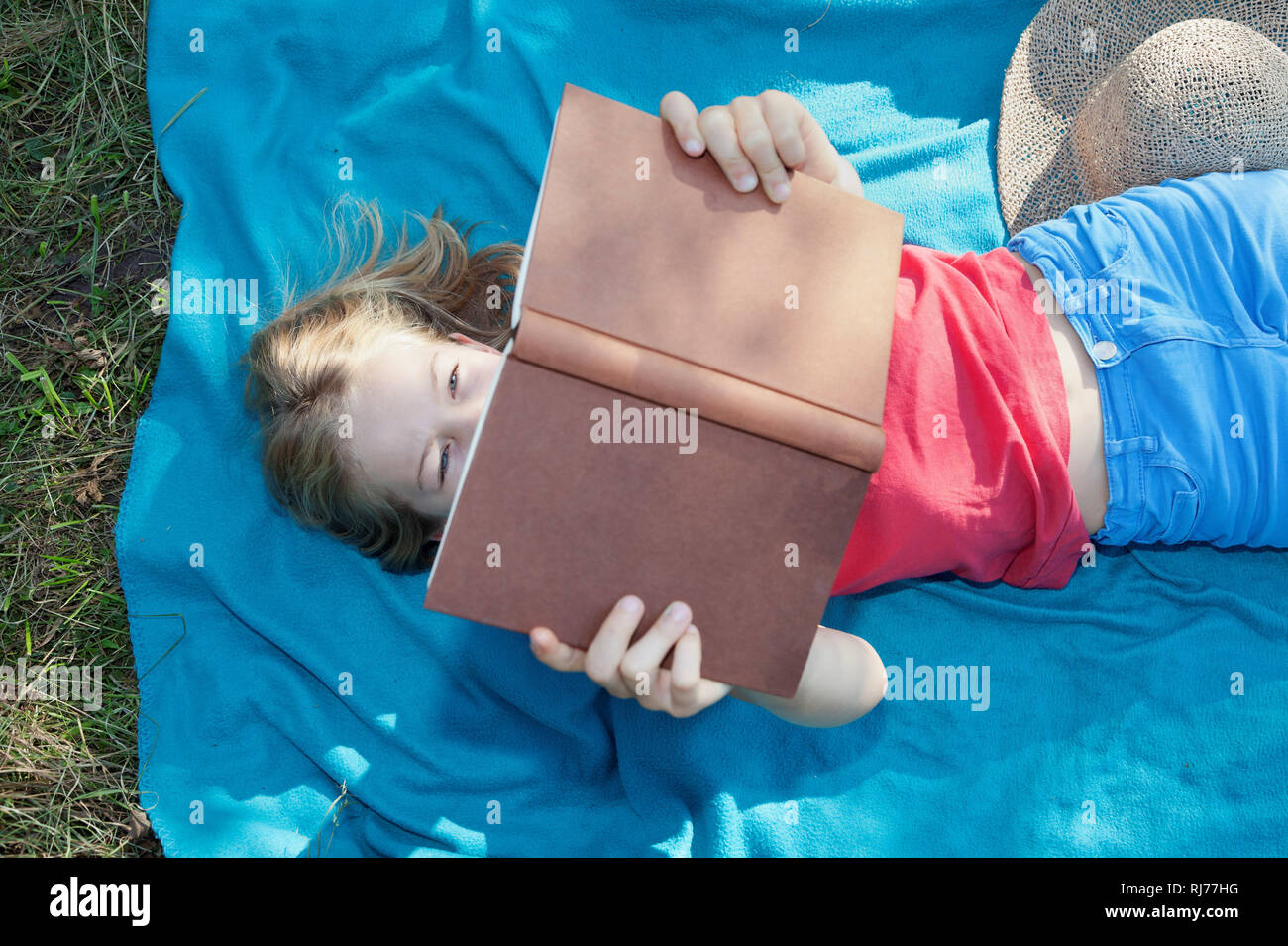 Neunjähriges Mädchen liegt auf einer Decke und liest ein Buch Stock Photo