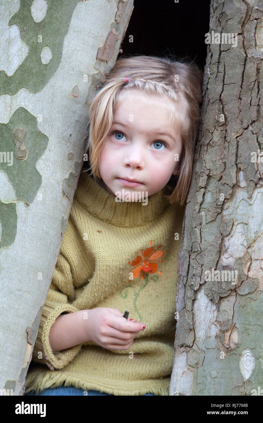Sechsjähriges Mädchen mit nachdenklichem Blick sitz in einem hohlen Baum Stock Photo