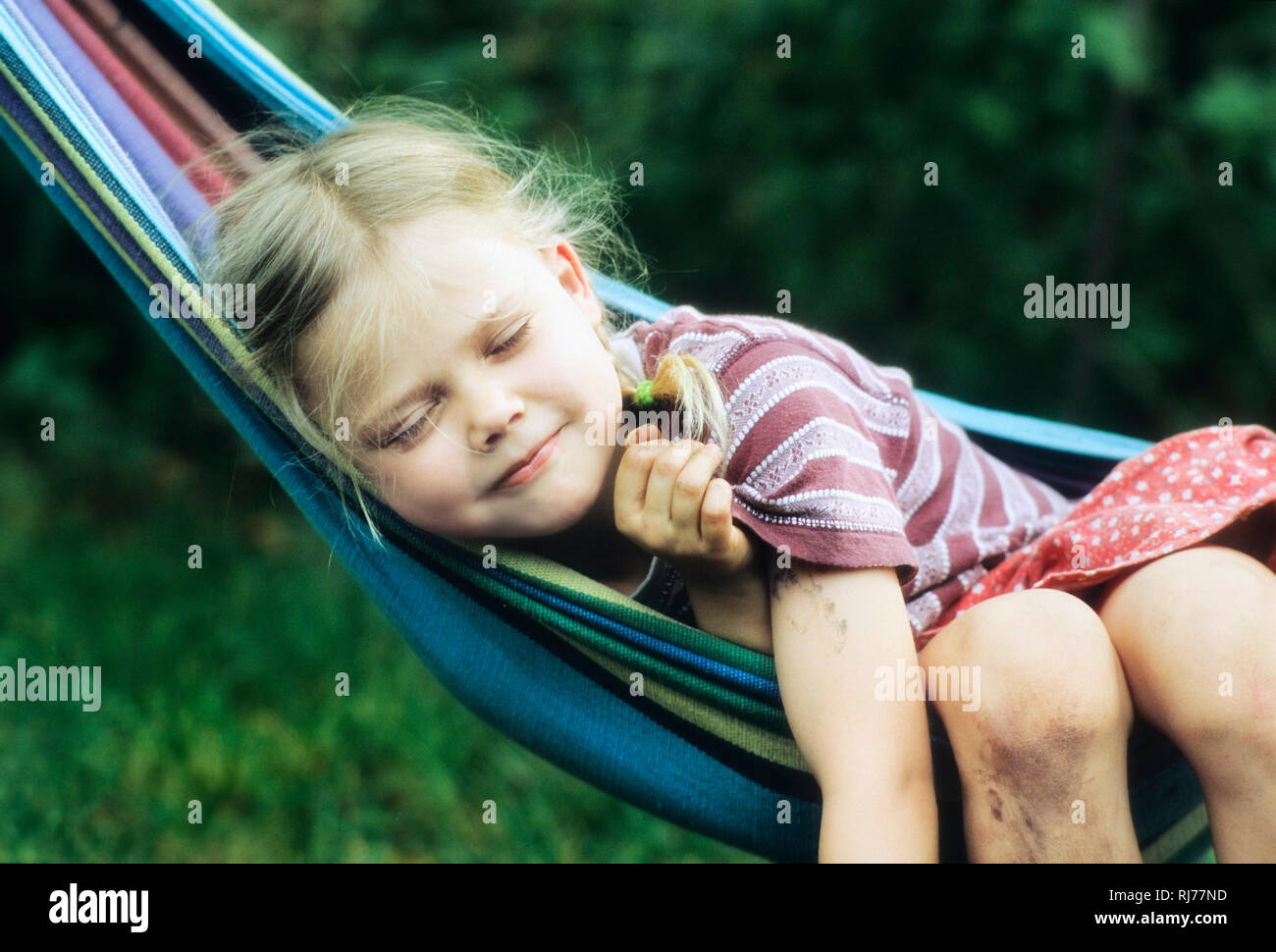 Mädchen, 6 Jahre alt, vom Spielen verschmutzt, liegt mit einem zufriedenen Lächeln in einer Hängematte Stock Photo