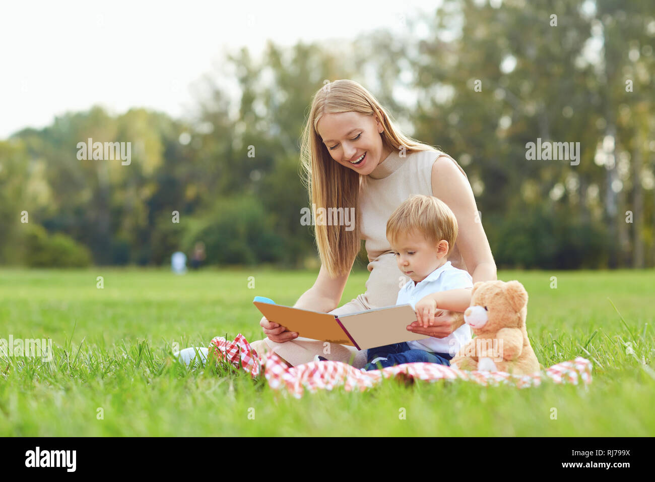 Mother with child reads on the grass in the park.  Stock Photo