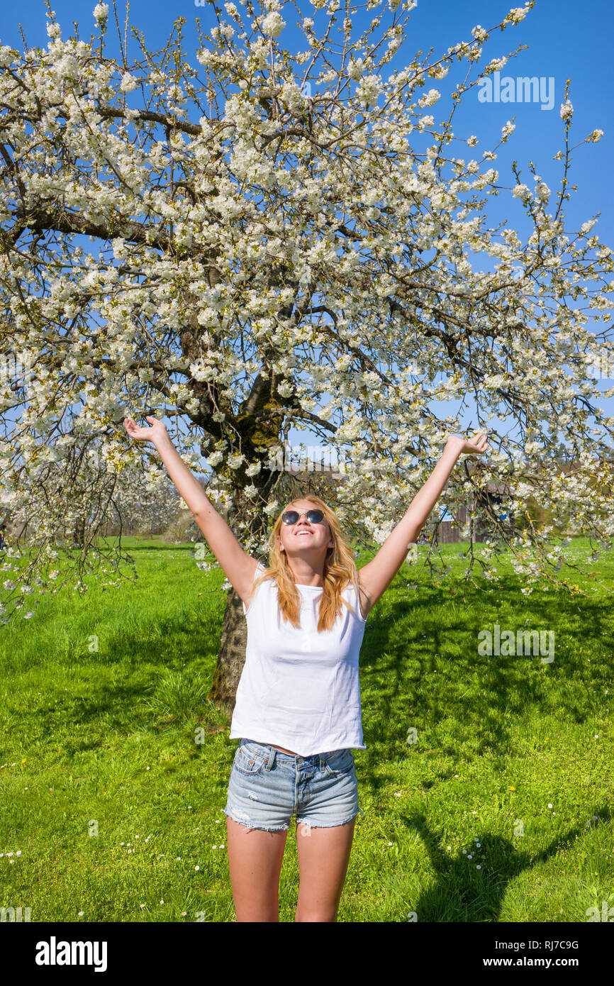 junge Frau steht mit ausgestreckten Armen unter blühendem Baum, Stock Photo