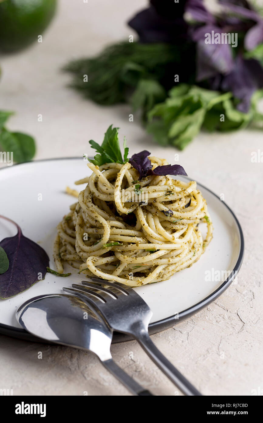 Italian pasta spaghetti with basil pesto and fresh herbs at white plate at white background Stock Photo