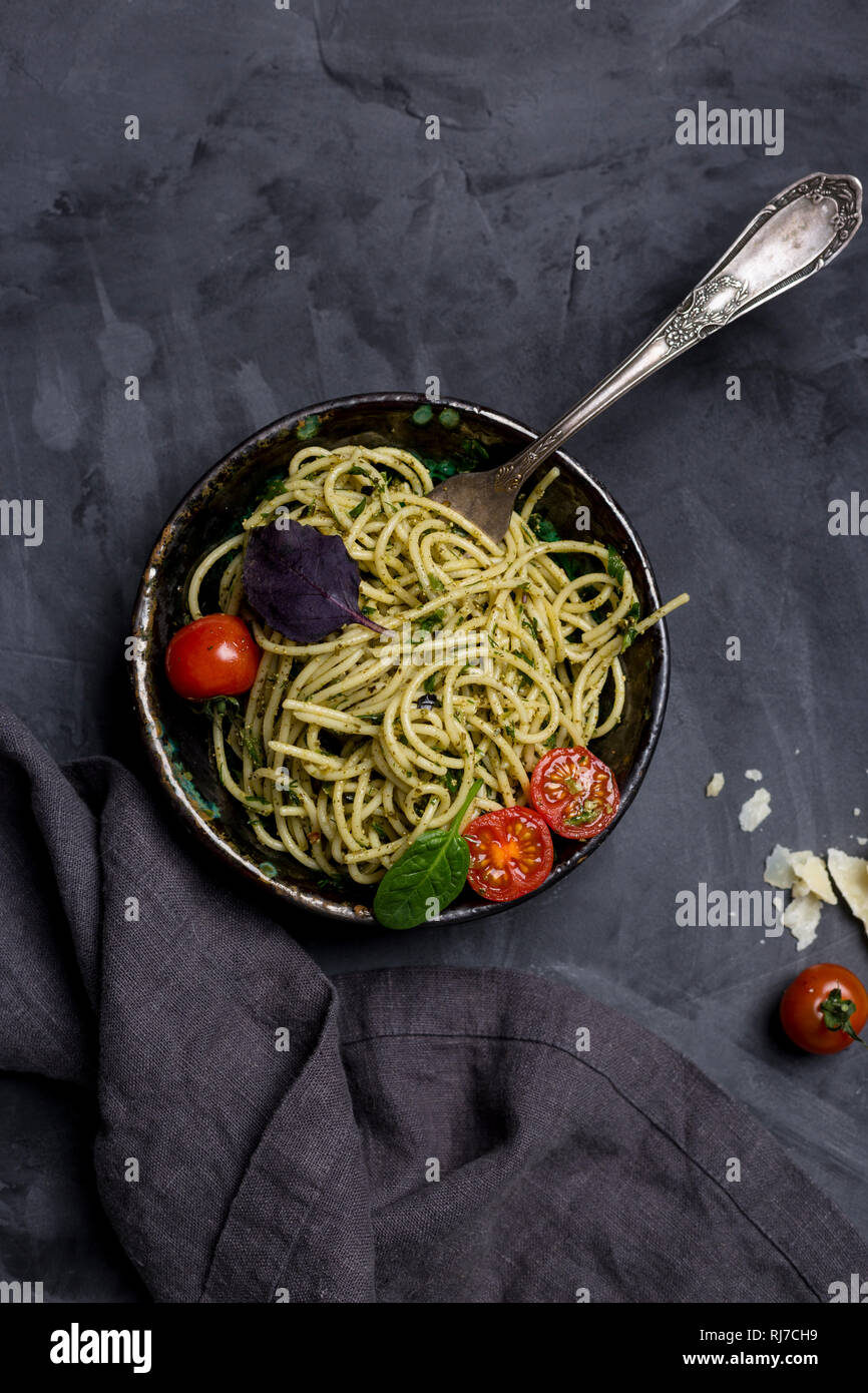 Pasta with pesto in bowl with fork at dark background. Cheese, cherry tomatoes and napkin near. Concept of Italian food. Top view Stock Photo
