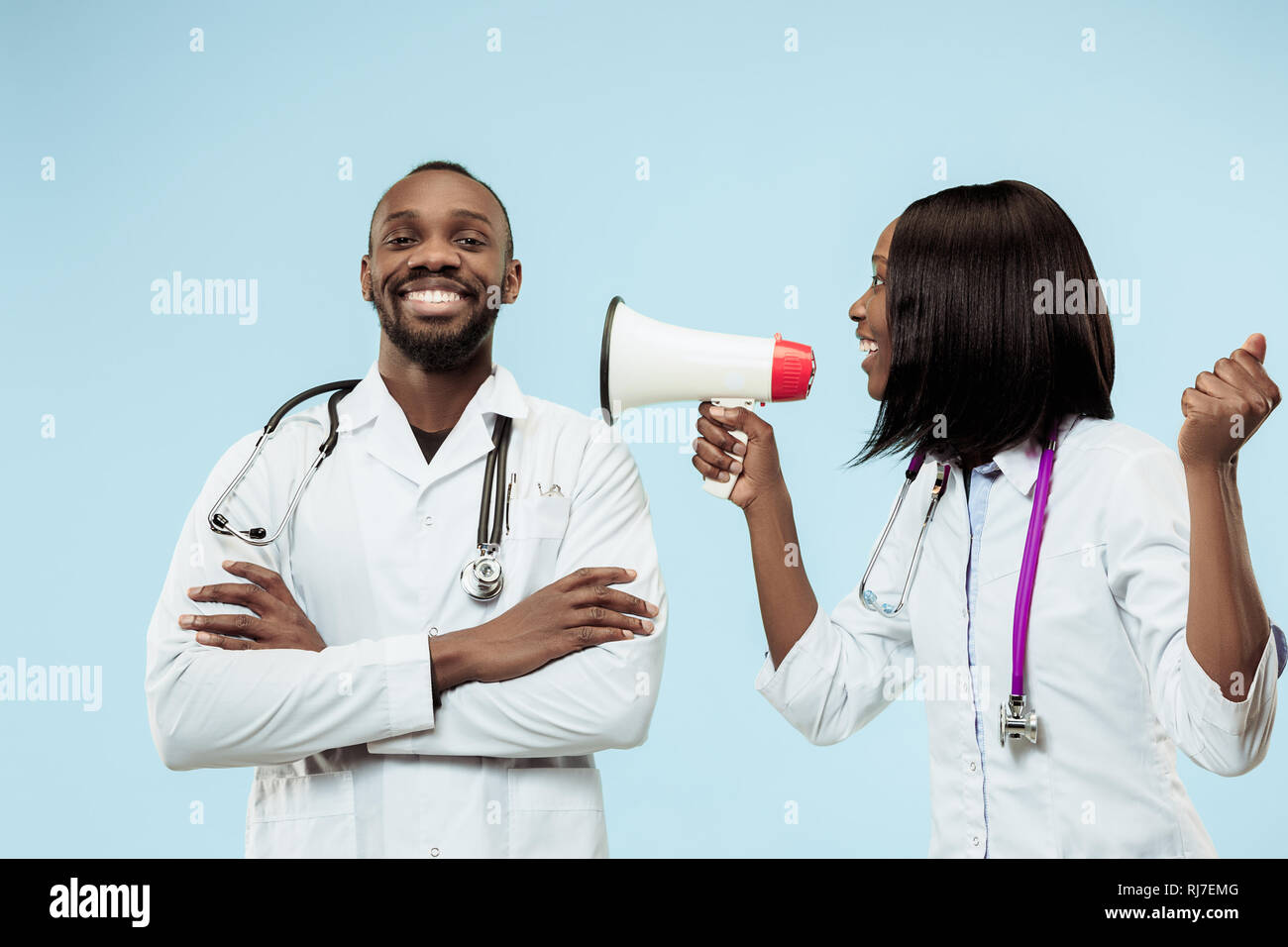 The female and male smiling happy afro american doctors on blue background at studio with megaphone. The clinic, medical, nurse, health, healthcare, hospital, care, job, professional concept Stock Photo