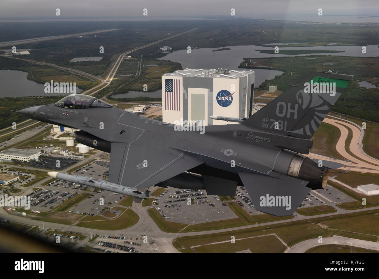 An F-16 Fighting Falcon, assigned to the 180th Fighter Wing, Ohio Air National Guard, flies over the Vehicle Assembly Building at the Kennedy Space Center during a deployment to Patrick Air Force Base, Feb. 4, 2019. The 180FW deployed more than 130 Airmen to Patrick AFB to develop and enhance interoperability, force integration and understanding of our sister service units. (Air National Guard photo by Senior Airman Hope Geiger) Stock Photo