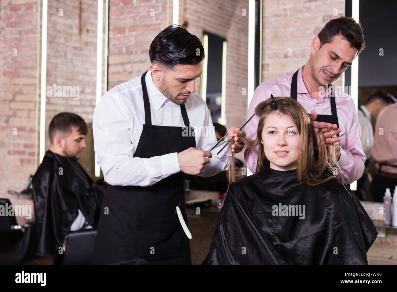 Two skilled men hairdressers making hairstyle for young female client in hair studio Stock Photo