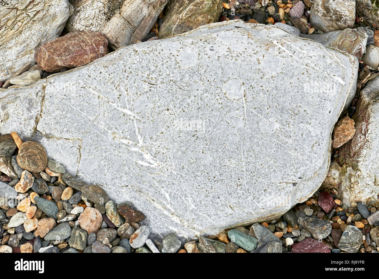 Big flat, roundish, gray colored stone, framed by other smaller stones and pebbles at a coastline in the Philippines. Ideal for placing text on it. Stock Photo