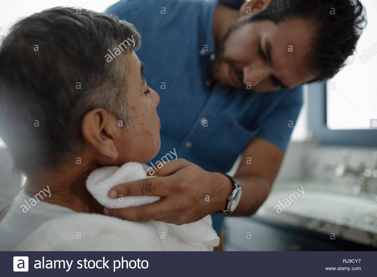 Latinx son shaving senior father s face Stock Photo