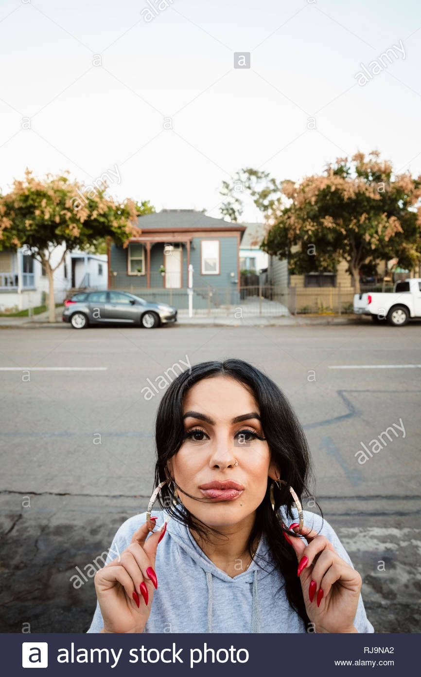 Portrait confident Latinx young woman with hoop earrings on neighborhood sidewalk Stock Photo
