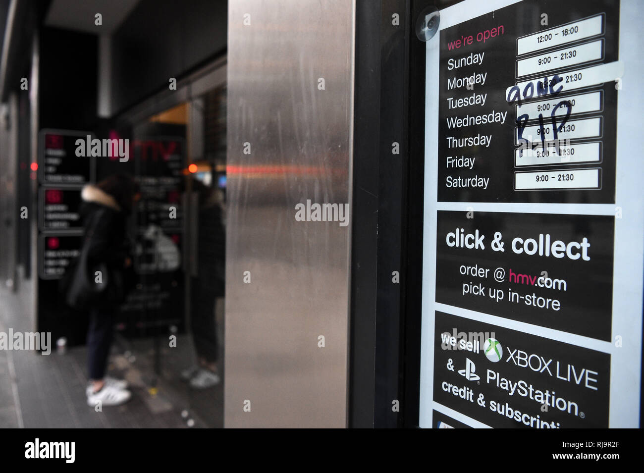A woman looks through the shutters and a 'Gone RIP' message written on the  opening hours of the HMV flagship store on Oxford Street in London, which  is among those to have