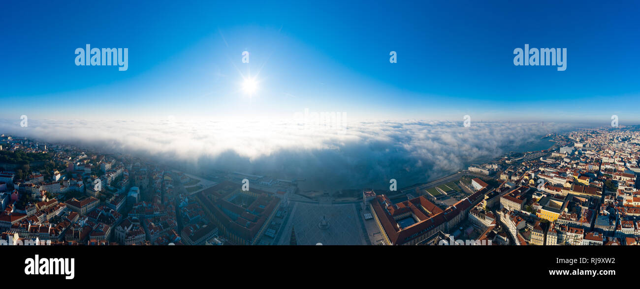 Aerial; panoramic drone view of foggy Lisbon morning; impending clouds over the ancient ginger roofs; blue skyline and bright sun in portuguese histor Stock Photo