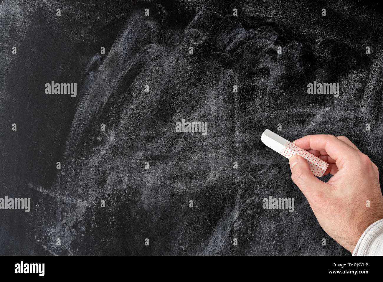 hand holding piece of chalk against empty dusty blackboard Stock Photo