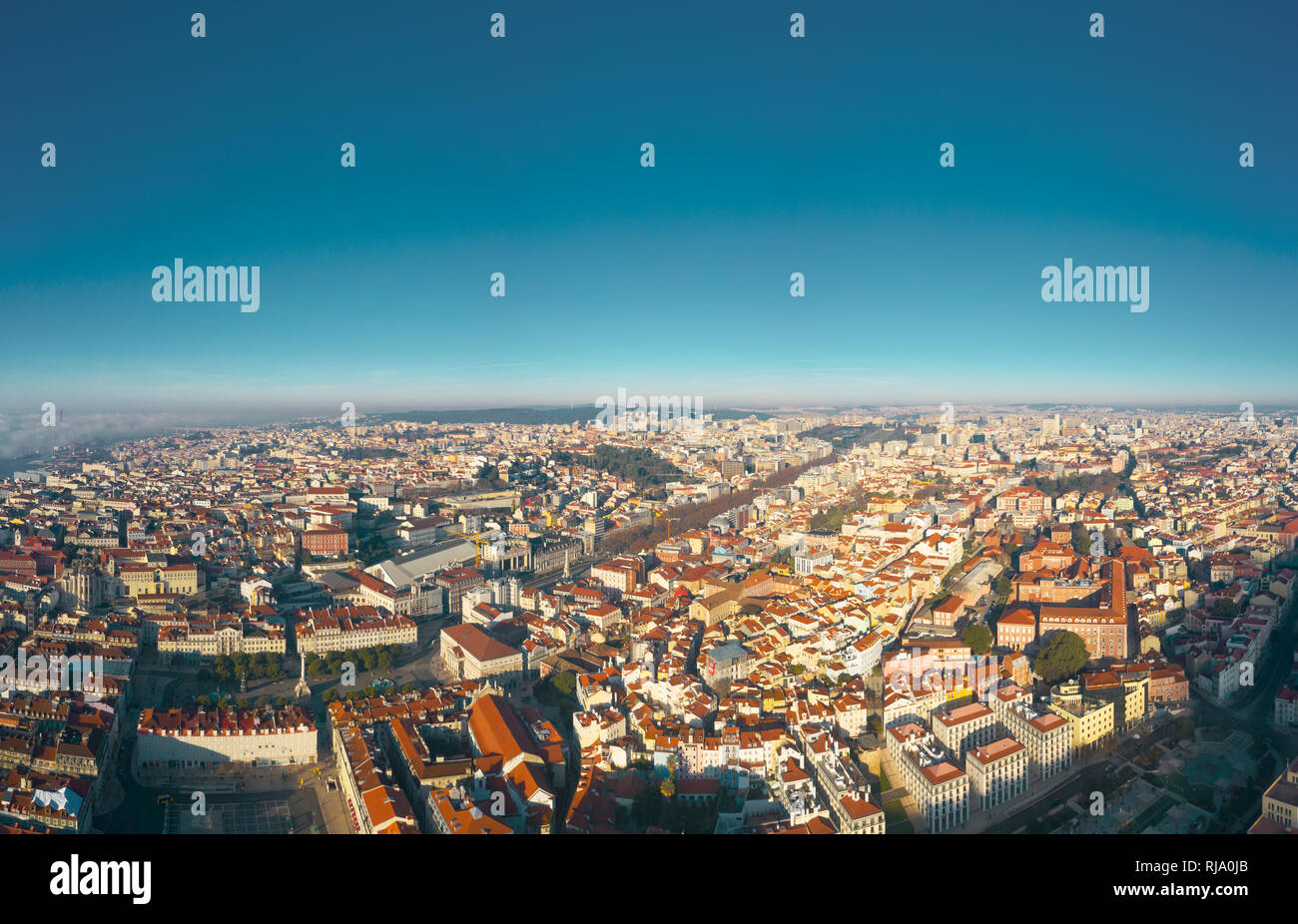 Aerial; panoramic drone view of foggy Lisbon morning; impending clouds over the ancient ginger roofs; blue skyline and bright sun in portuguese histor Stock Photo