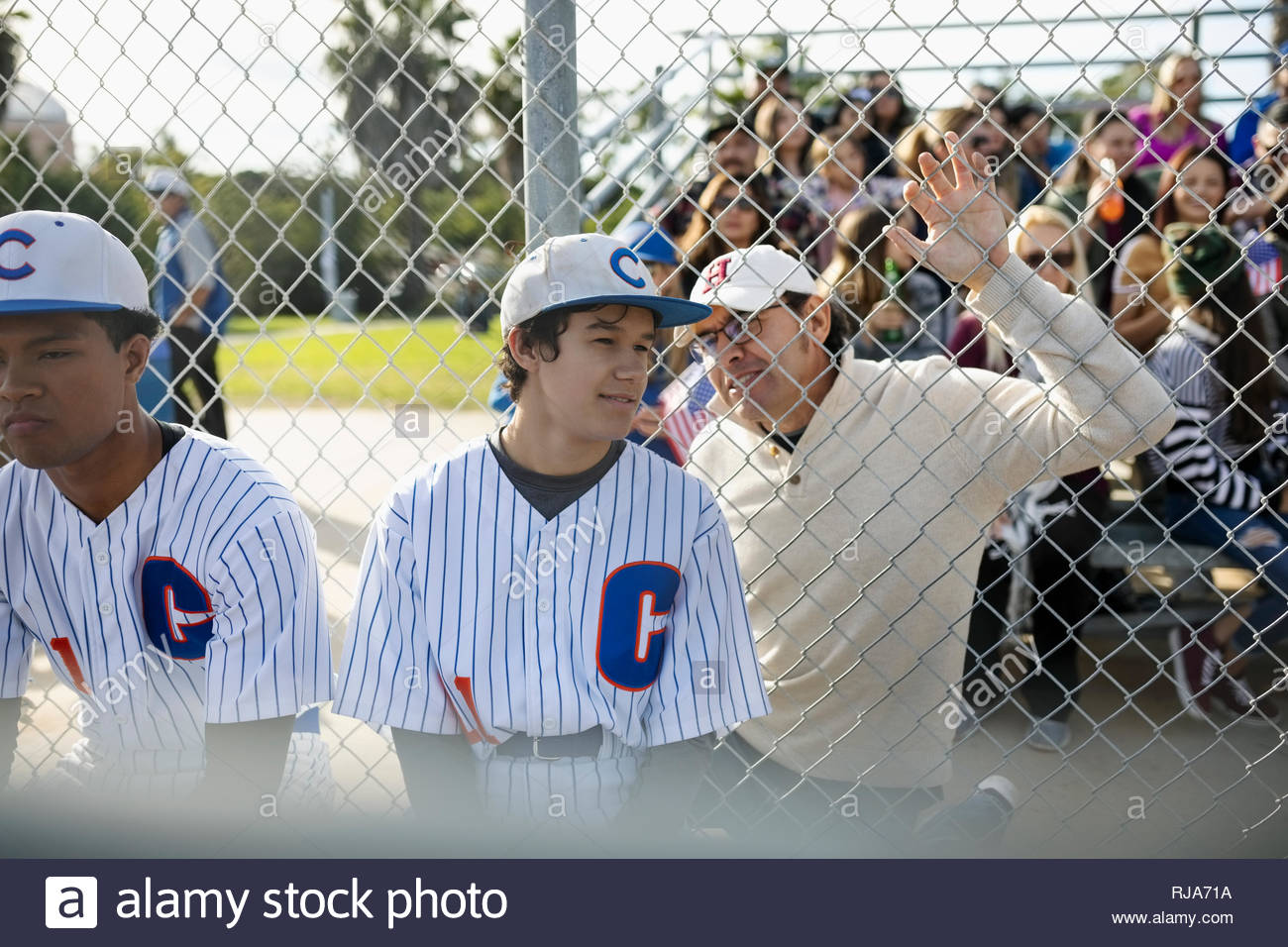 Latinx father talking to baseball player son at fence Stock Photo