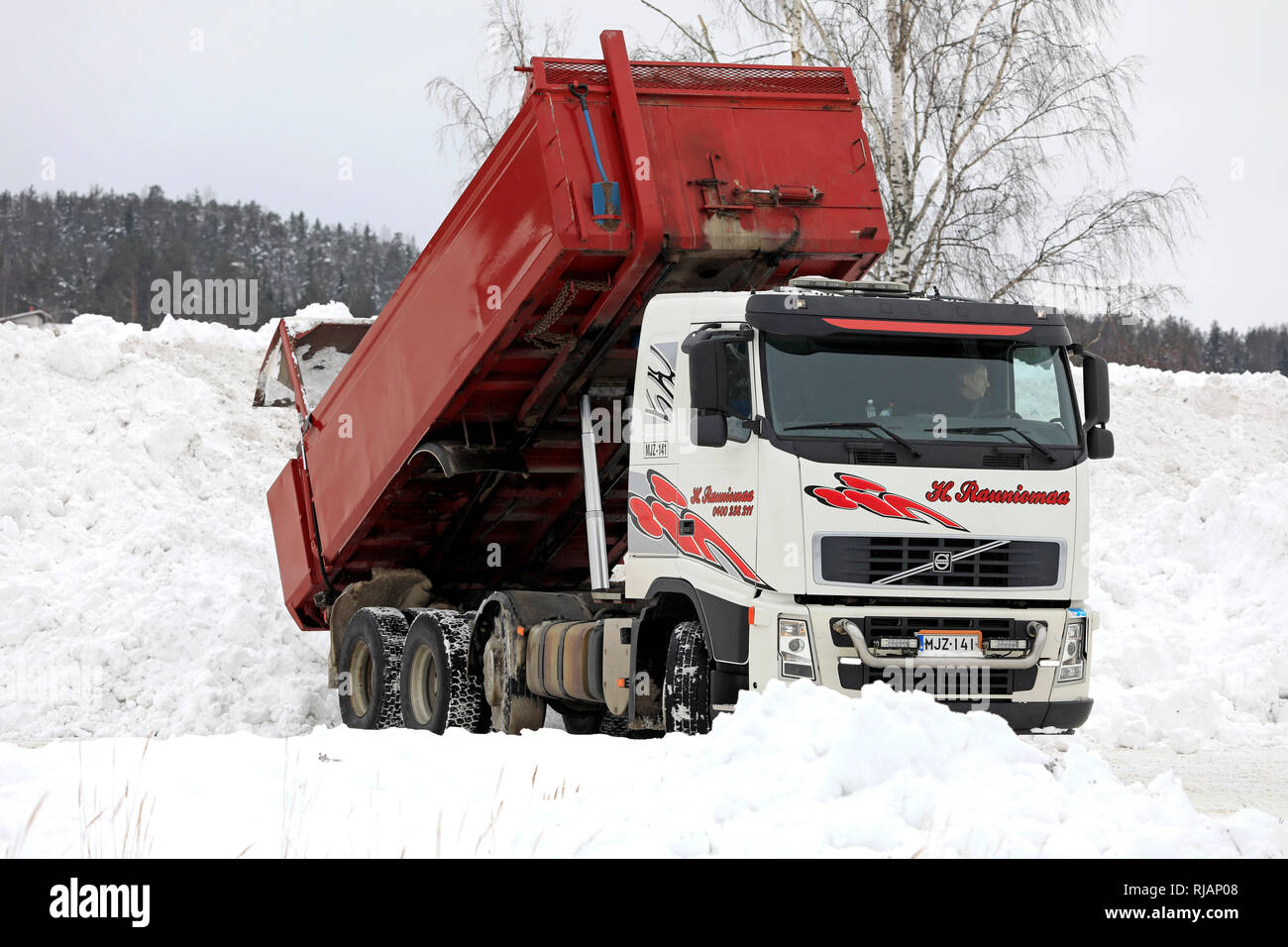 Salo, Finland - February 2, 2019: Volvo tipper truck unloads snow cleared from streets and parking lots at municipal snow dumping area. Stock Photo