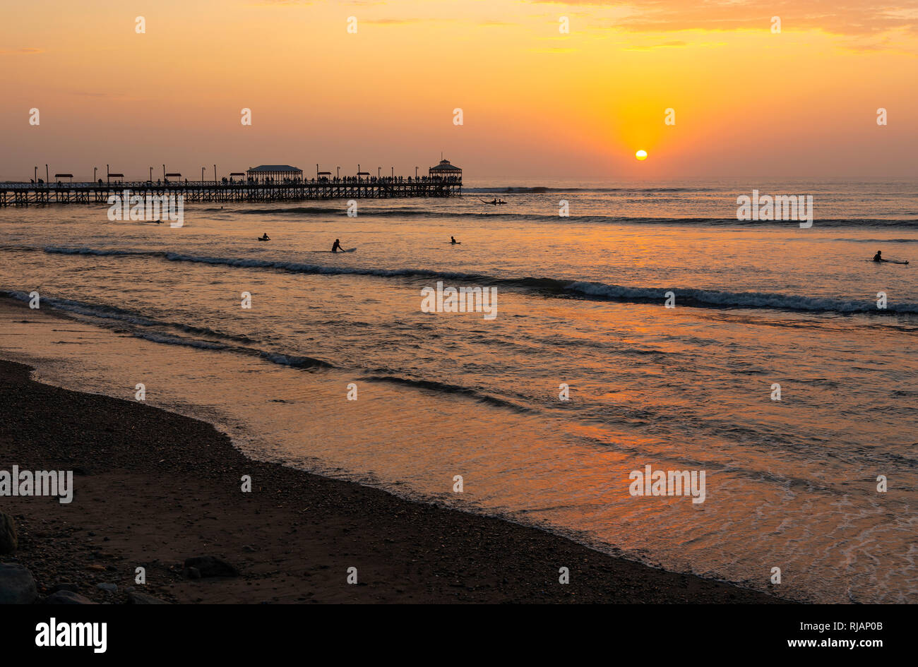 The wooden pier of Huanchaco beach near Trujillo with the silhouette of surfers at sunset, Peru. Stock Photo