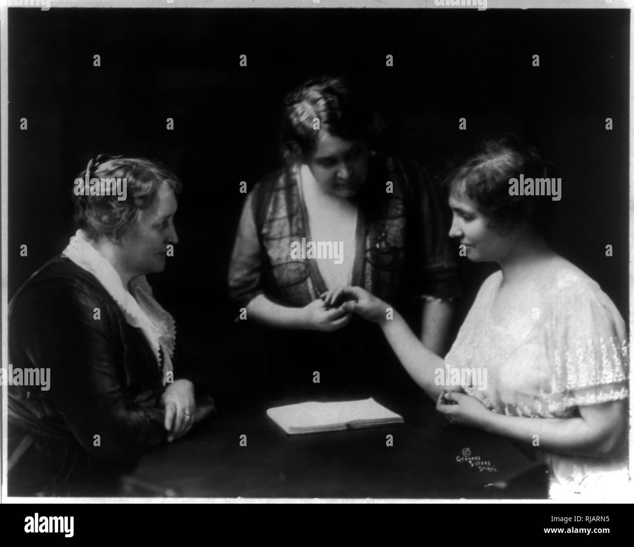 Helen Keller reading a woman's fingers as another woman watches1914  Helen Keller (1880 – 1968), American author, political activist, and lecturer. She was the first deaf-blind person to earn a bachelor of arts degree. she campaigned for women's suffrage, labour rights, socialism, antimilitarism, and other similar causes. Stock Photo