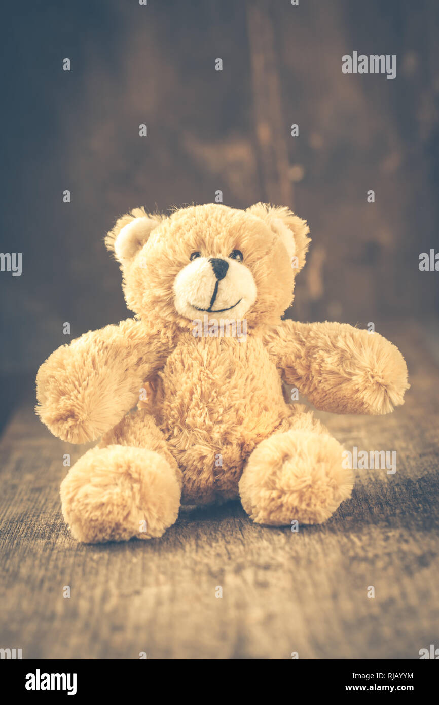 Ein kleiner Teddy sitzt auf einem dunklen Holztisch, Stock Photo