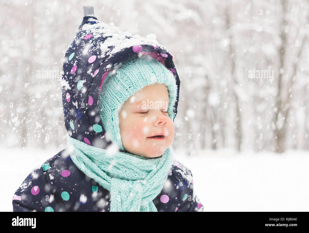 Baby in a winter jumpsuit rejoices in the first snow Stock Photo