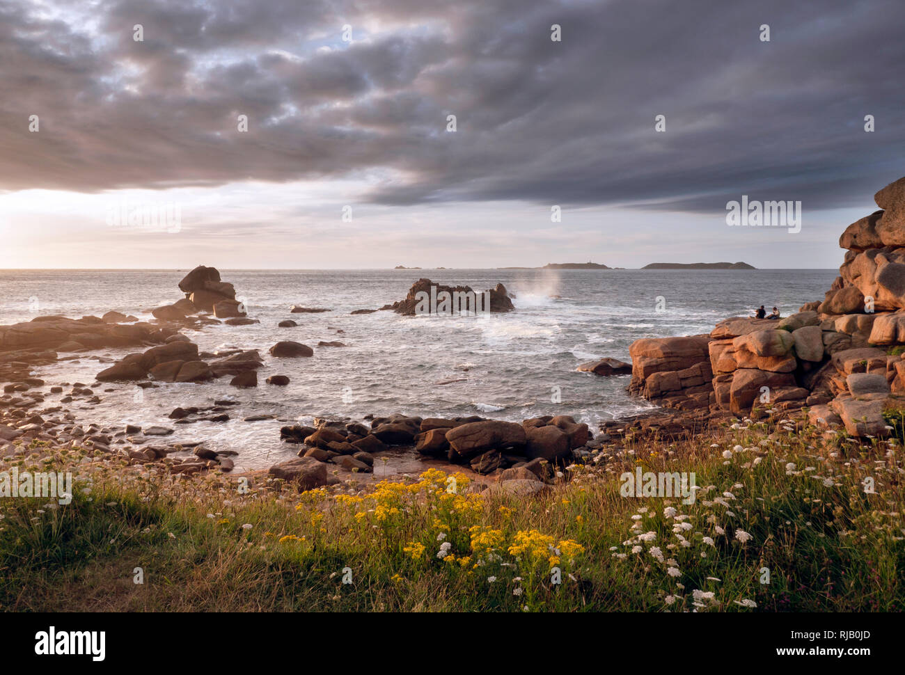 Die Côte de Granit Rose mit imposanten, rosafarbenen Granitfelsen bei Ploumanach, zwei Personen beobachten den Sonnenuntergang Stock Photo