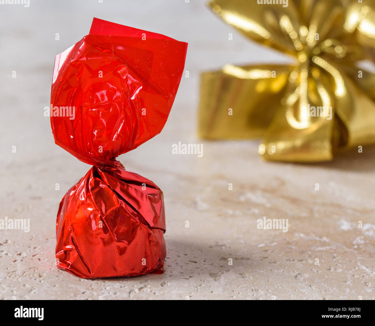 A cherry chocolate bonbon wrapped in red paper with a golden bow tie ribbon in the background. Stock Photo
